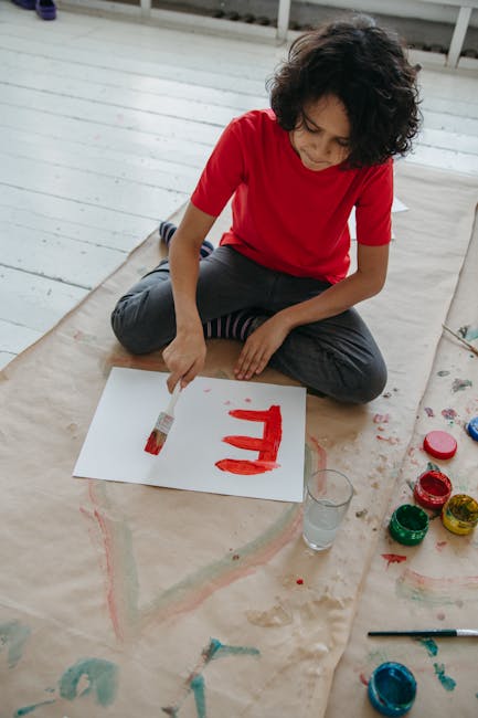 Child painting on paper with red paint indoors, showing creative arts and crafts activity.