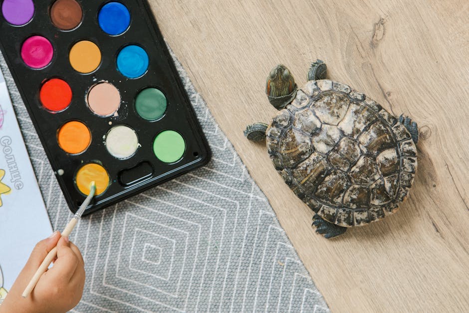 A turtle on a wooden floor beside a child painting with watercolors.